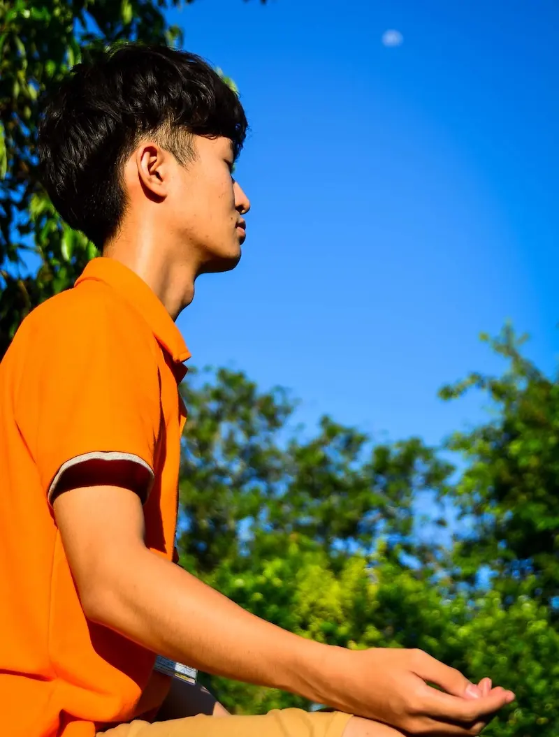A young man in an orange shirt sitting quietly in meditation