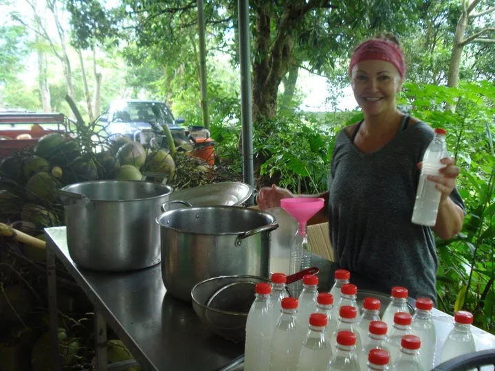 A smiling volunteer with bottles and cooking pots beside a coconut harvest