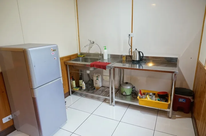 A simple kitchen with a refrigerator, sink and preparation table