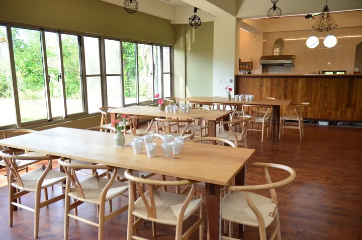 Wooden dining tables, a kitchen counter and large windows overlooking the garden