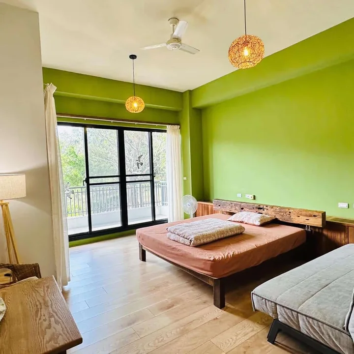A light guest room with a green wall, wooden furniture and a balcony door